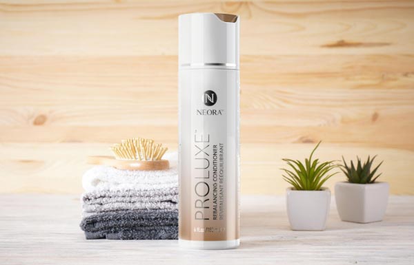 Image of ProLuxe Rebalancing Conditioner bottle beside two succulent plants and towels.