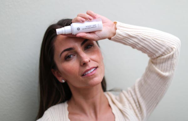 A woman holding the Hydrating Facial Mist in front of her face.